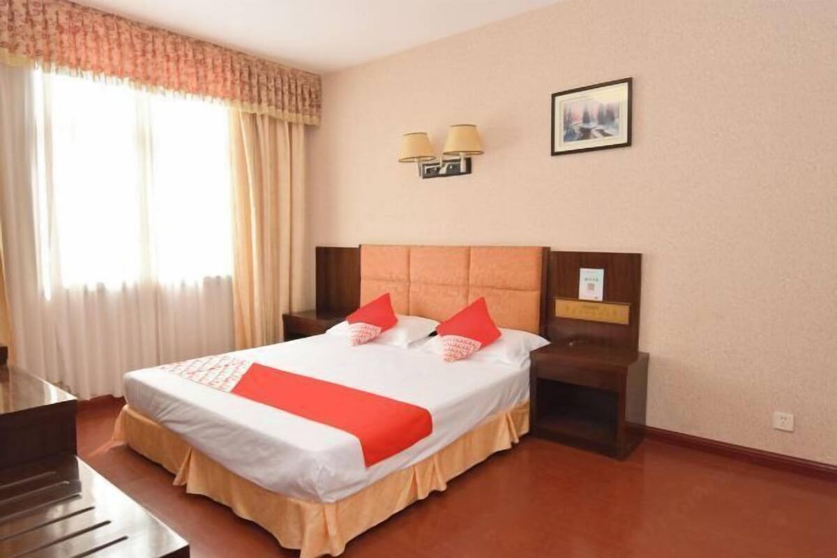 Een hotelkamer met een bed, nachtkastje, lamp en een schilderij aan de muur.