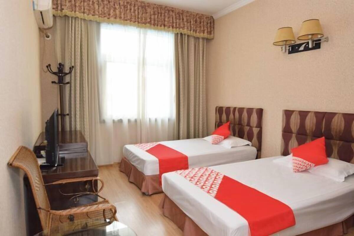 Hotelkamer met twee bedden, een bureau, een stoel, een televisie en een raam met gordijnen.