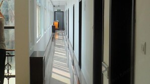 A long, narrow hallway with a series of doors on one side and windows on the other, leading to a reception area at the end. - Jinse Hepan Business Hotel (Tongcheng)