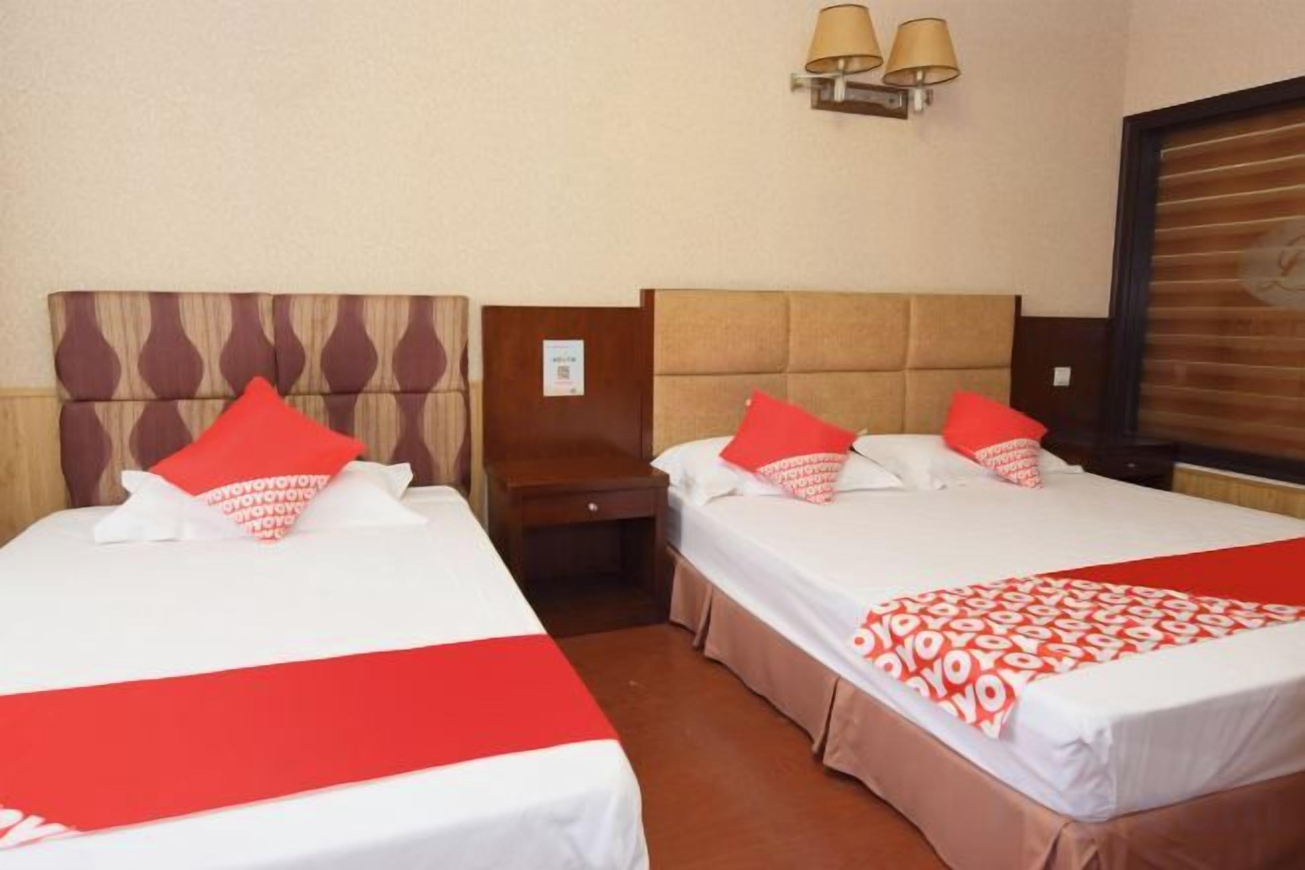 Een hotelkamer met twee bedden, elk voorzien van een rode en witte spreideken, een houten hoofdeinde en een nachtkastje ertussen.