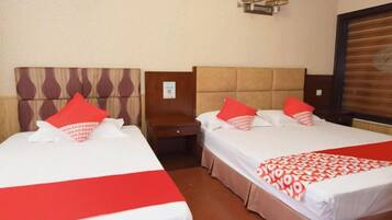 Een hotelkamer met twee bedden, elk voorzien van een rode en witte spreideken, een houten hoofdeinde en een nachtkastje ertussen.