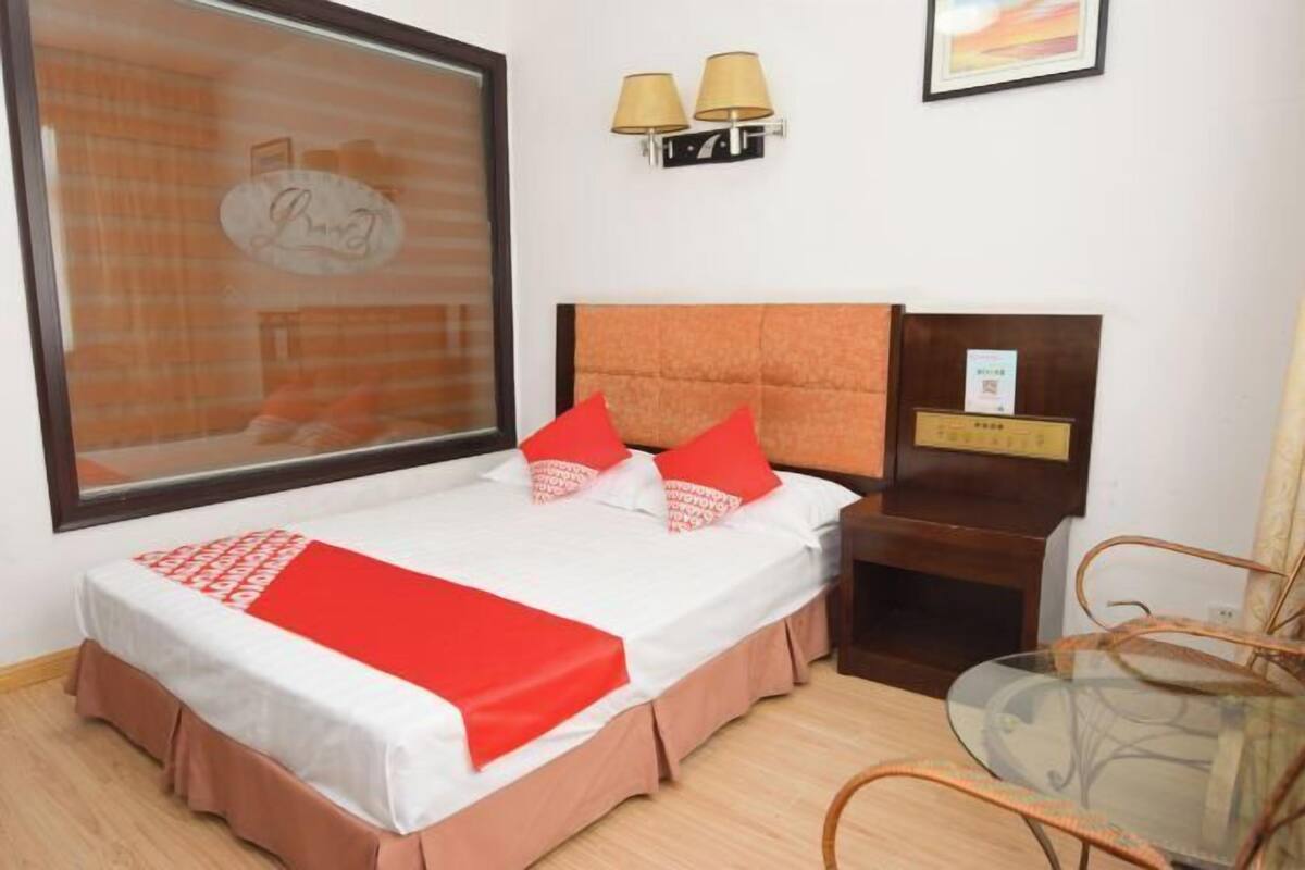 Een hotelkamer met een bed, nachtkastje, lamp en een raam met jaloezieën.