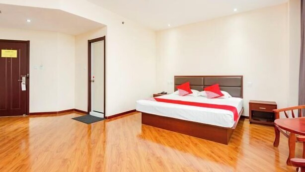 A hotel room with a wooden floor, a bed with red pillows, a nightstand, and a chair. - Jinse Hepan Business Hotel (Tongcheng)