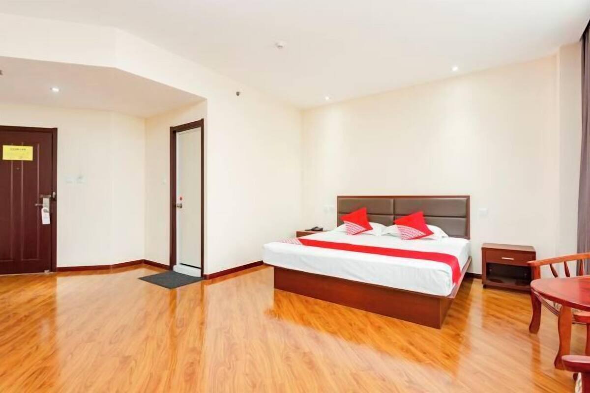 Een hotelkamer met een houten vloer, een bed met rode kussens, een nachtkastje en een stoel.