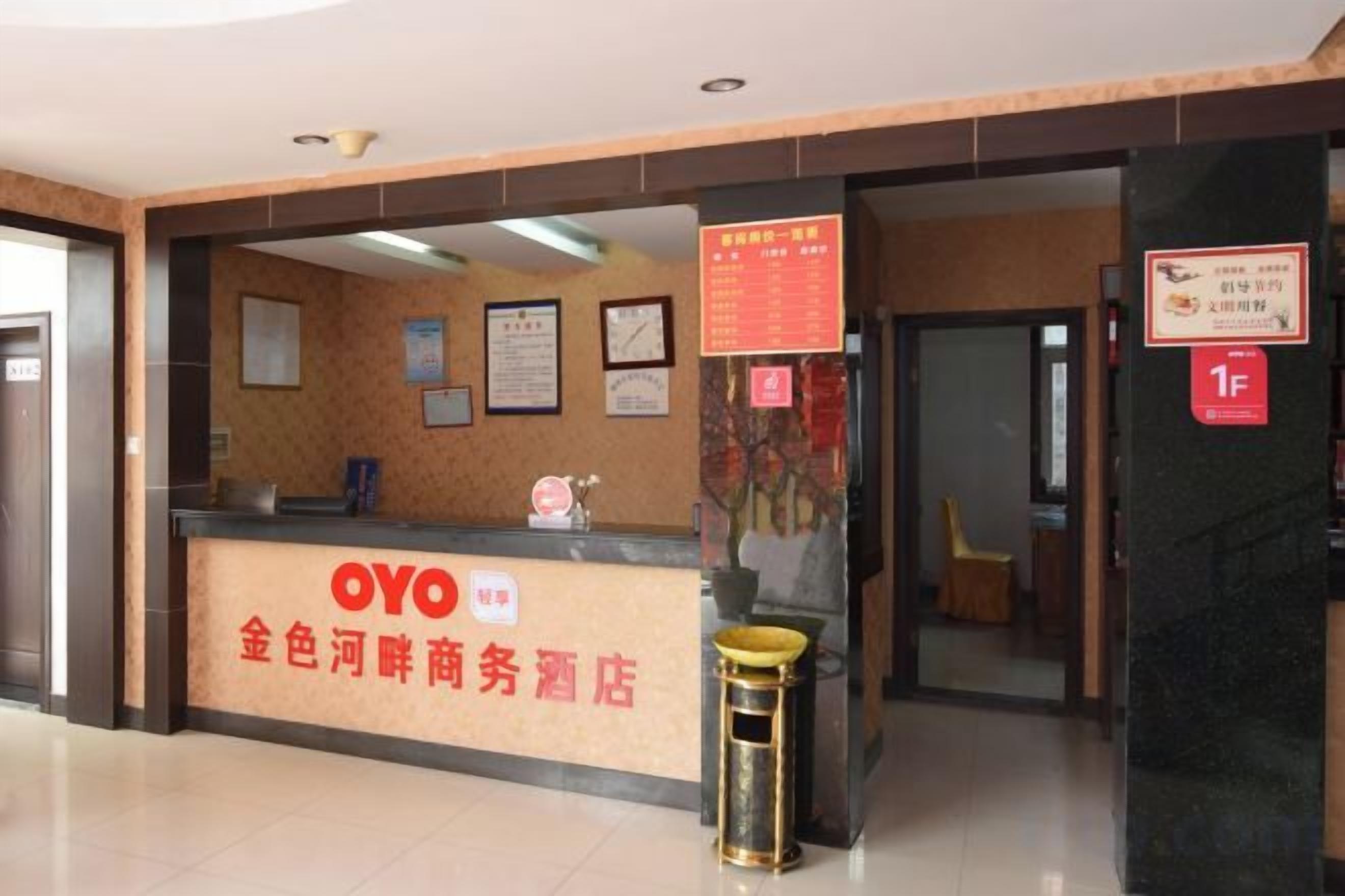 Een hotel receptiebalie met een bord voor OYO hotel, een prullenbak en een muur met ingelijste certificaten.