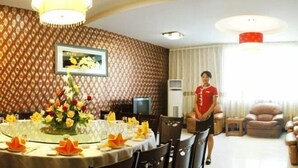 A dining area with a round table set for a meal, a television, and a patterned wall. - Jinse Hepan Business Hotel (Tongcheng)