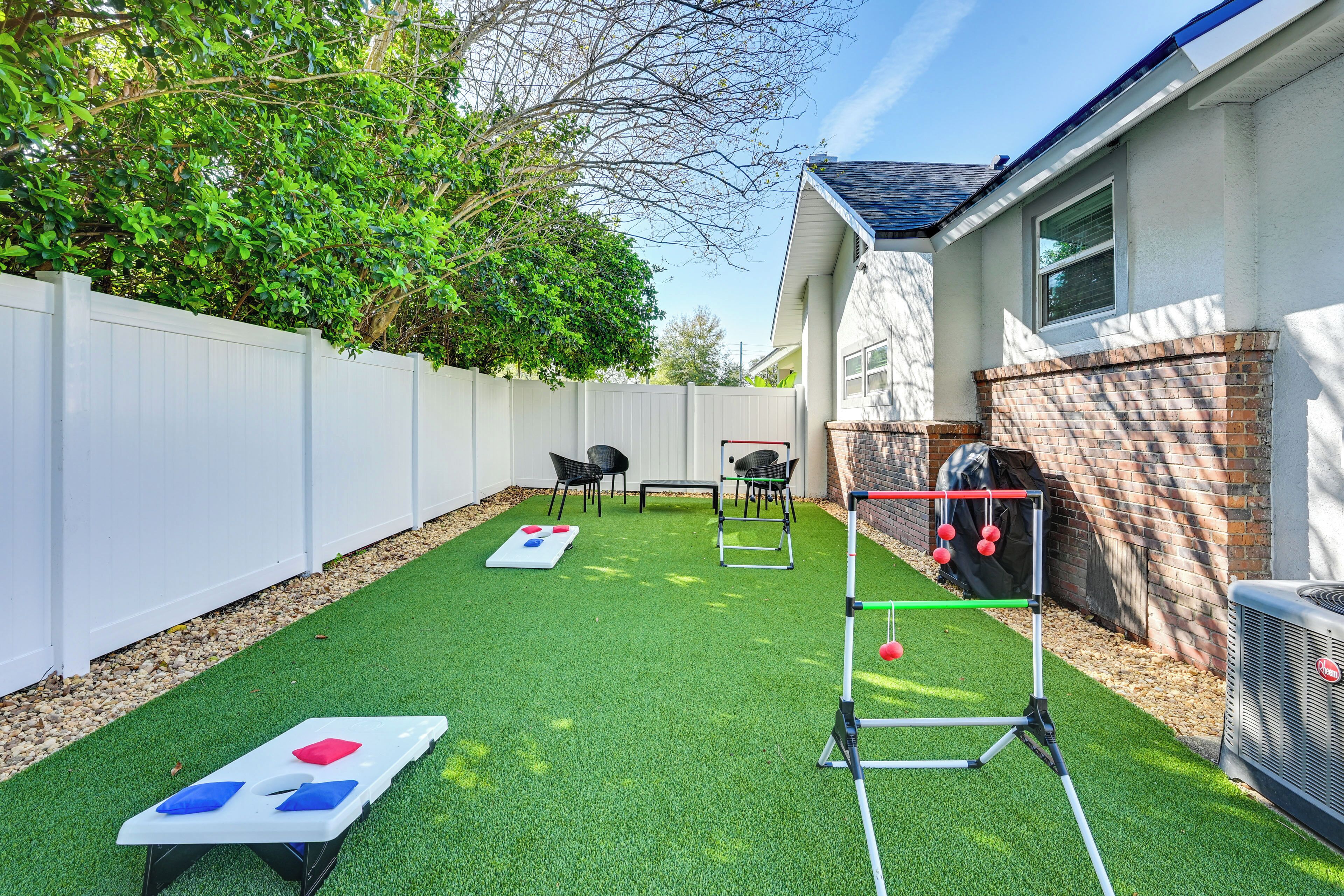 A backyard with artificial grass, a white fence, a brick wall, and outdoor furniture.