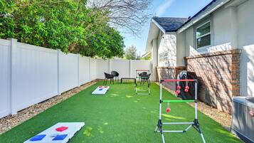 A backyard with artificial grass, a white fence, a brick wall, and outdoor furniture.