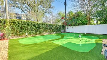 Ein Minigolfplatz mit zwei Bahnen, umgeben von einer Hecke und Bäumen.