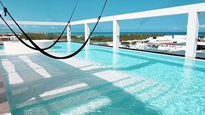 A rooftop infinity pool with a hammock, white pillars, and a view of the ocean and cityscape. - Cozy studio in fabulous Playa del Carmen just a few steps to beach, gym, WiFi (Playa del Carmen)