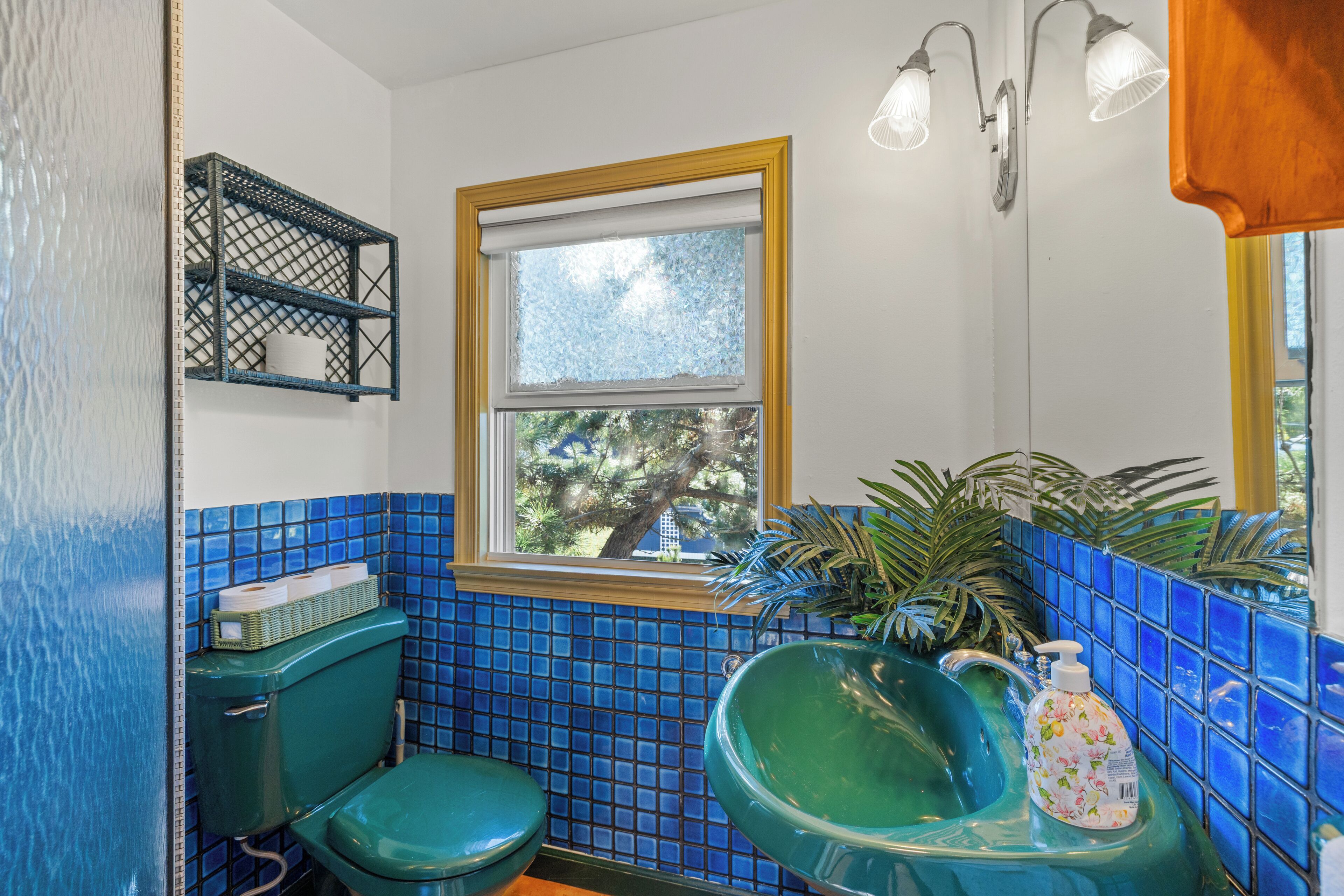 A bathroom with a green toilet, a sink with a green basin, and a window with a view of trees.