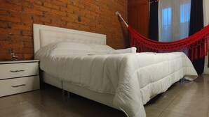 A bedroom with a white bed, a nightstand, a red hammock, and a brick wall. - House in Santa Rosa de Cabal (Santa Rosa de Cabal)