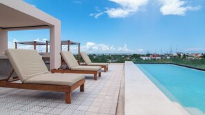 A poolside area with lounge chairs and a view of the cityscape. - Bright 1 Bedroom with balcony, Gym, WiFi, Infinity Pool at Roof top (Playa del Carmen)
