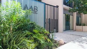 A modern building with a gated entrance, surrounded by lush greenery and a clear sky. - Bright 1 Bedroom with balcony, Gym, WiFi, Infinity Pool at Roof top (Playa del Carmen)