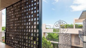 A modern building with a grid-patterned facade, a tree sculpture, and a balcony with a metal railing. - Bright 1 Bedroom with balcony, Gym, WiFi, Infinity Pool at Roof top (Playa del Carmen)