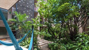 A courtyard with a hammock, steps leading to a building, and lush greenery. - Bright 1 Bedroom with balcony, Gym, WiFi, Infinity Pool at Roof top (Playa del Carmen)