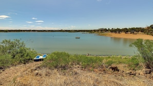 A calm lake with a small boat docked on the shore, surrounded by greenery and a sandy beach. - Firelit Nights By the Lake: Cozy Show Low Retreat (Show Low)