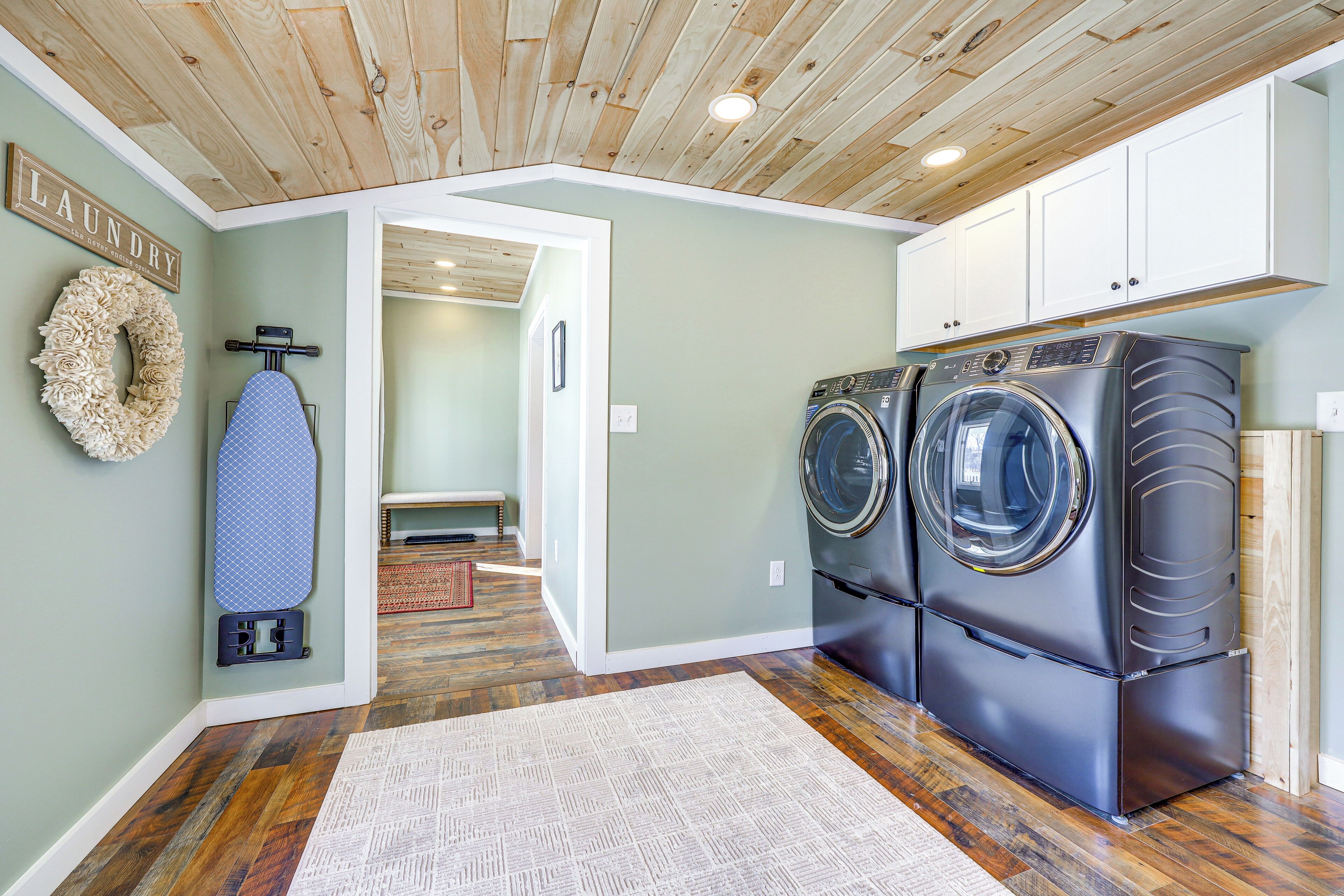 A laundry room with wooden flooring, a washing machine, a dryer, and a wall-mounted ironing board.