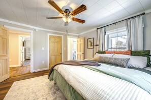 A bedroom with a bed, a ceiling fan, wooden doors, and a window with curtains.
