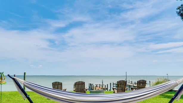 Een hangmat op een grasveld met uitzicht op het water en aanmerende stoelen.
