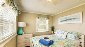 Slaapkamer met een bed, nachtkastje, lamp, raam met zonwering en een wanddecoratie.