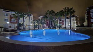 A swimming pool surrounded by palm trees and buildings with balconies.