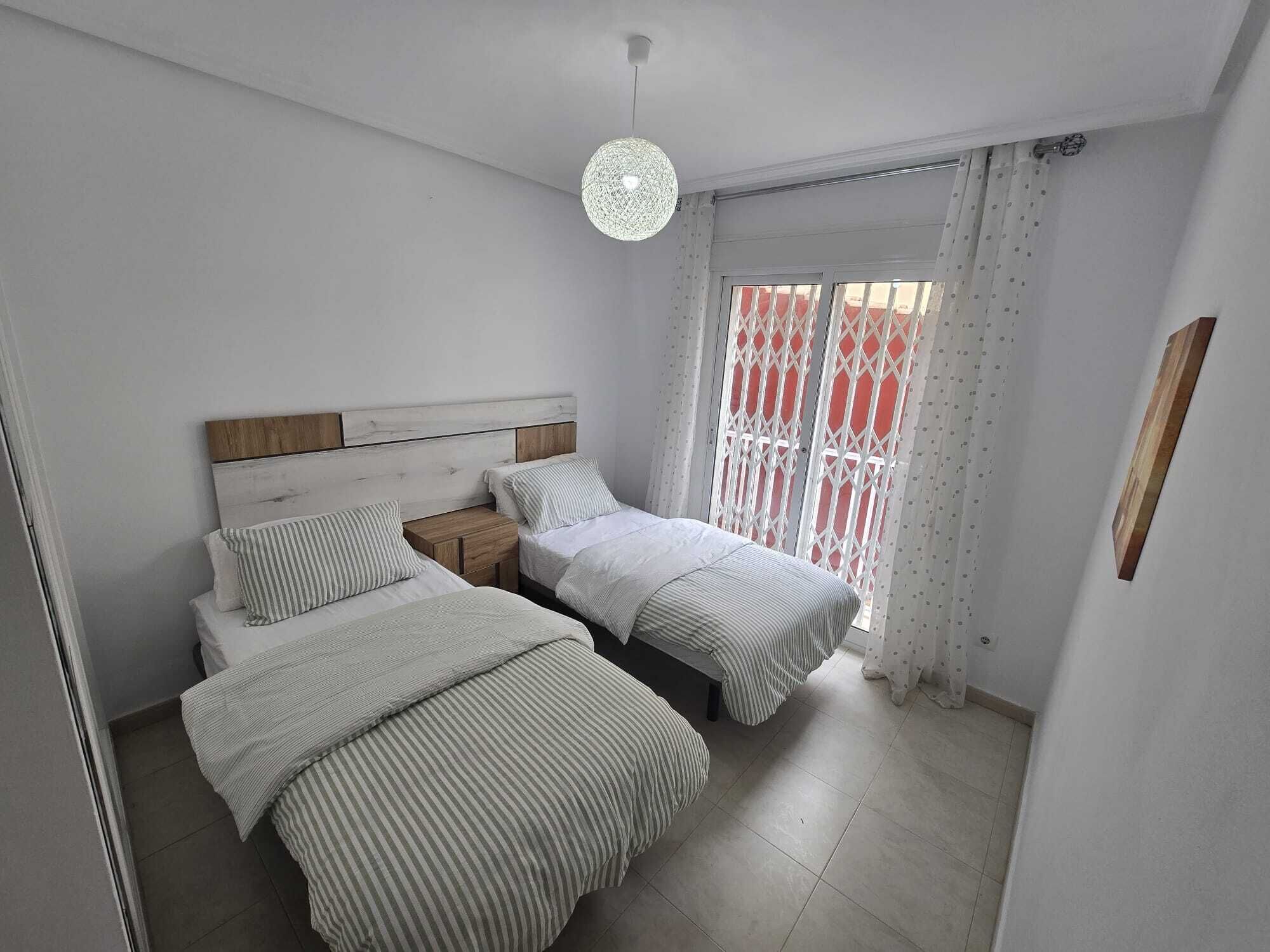 A bedroom with two beds, a wooden headboard, a hanging light fixture, and a window with a view.