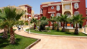 A residential building with balconies, a paved courtyard, and palm trees.
