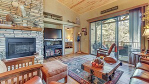 A cozy living room with a stone fireplace, leather furniture, and a large TV screen. - Rustic Retreat w/ Spacious Deck in Show Low! (Show Low)
