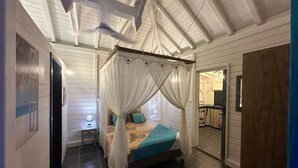 A bedroom with a four-poster bed, a ceiling fan, and a view into another room.