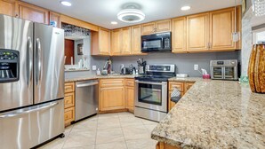A modern kitchen with stainless steel appliances, wooden cabinets, granite countertops, and a built-in microwave. - 8 Mi to Sunset Beach: Home w/ Large Patio + Pool! (New Port Richey)