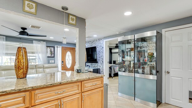 A modern kitchen with wooden cabinets, a granite countertop, and a built-in wine refrigerator. - 8 Mi to Sunset Beach: Home w/ Large Patio + Pool! (New Port Richey)