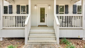 Una escalera de madera blanca que lleva a una puerta con panel de vidrio, flanqueada por dos barandillas blancas con contraventanas negras.