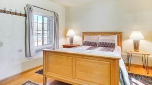 A bedroom with a wooden bed, two bedside lamps, a window with curtains, and a small table with a lamp. - Peaceful & Historic Home in Patagonia! (Patagonia)