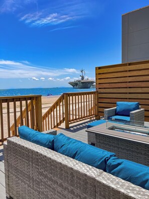 A deck with wicker furniture and a view of the ocean and an aircraft carrier.