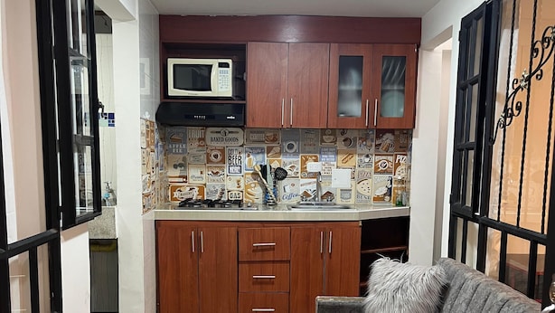 A compact living space with a kitchenette, a sofa, a small round table, and a patterned floor.