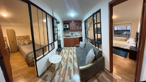 A compact living space with a sofa, a small round table, a kitchenette, and a bed.