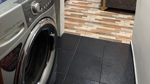 A compact kitchen with a washing machine, a refrigerator, and a window with curtains.