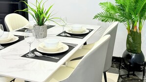 A modern dining area with a white table set for four, including plates, glasses, and cutlery. There is a potted plant on the table and a large mirror on the wall. - Modern with City view, 12 minutes from the beach (Dar es Salaam)