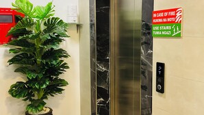 An elevator with a digital display, a fire safety sign, a potted plant, and a trash bin. - Modern with City view, 12 minutes from the beach (Dar es Salaam)