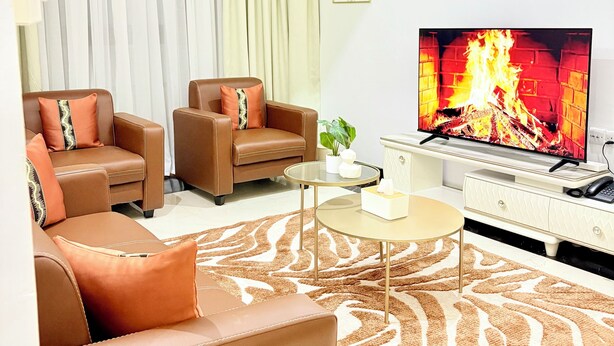 A modern living room with leather sofas, a television displaying a fire, and a ceiling fan. - Modern with City view, 12 minutes from the beach (Dar es Salaam)