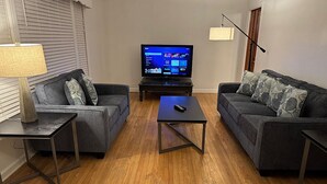 Ein Wohnzimmer mit zwei grauen Sofas, einem Couchtisch, einem Fernseher auf einem Schrank und einer Lampe auf einem Beistelltisch.