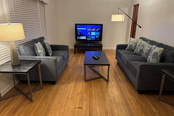 A living room with two grey sofas, a coffee table, a TV on a stand, and a lamp on a side table.