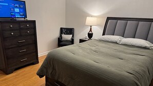 Ein ordentlich eingerichtetes Schlafzimmer mit einem Bett, einem Schminktisch, einem Sessel und einem Nachttisch mit Lampe.