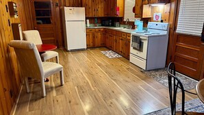 Eine kompakte Küche mit Holzausstattung, einem weißen Kühlschrank, einem Herd und einem Essbereich mit einem roten Tisch und zwei Stühlen.