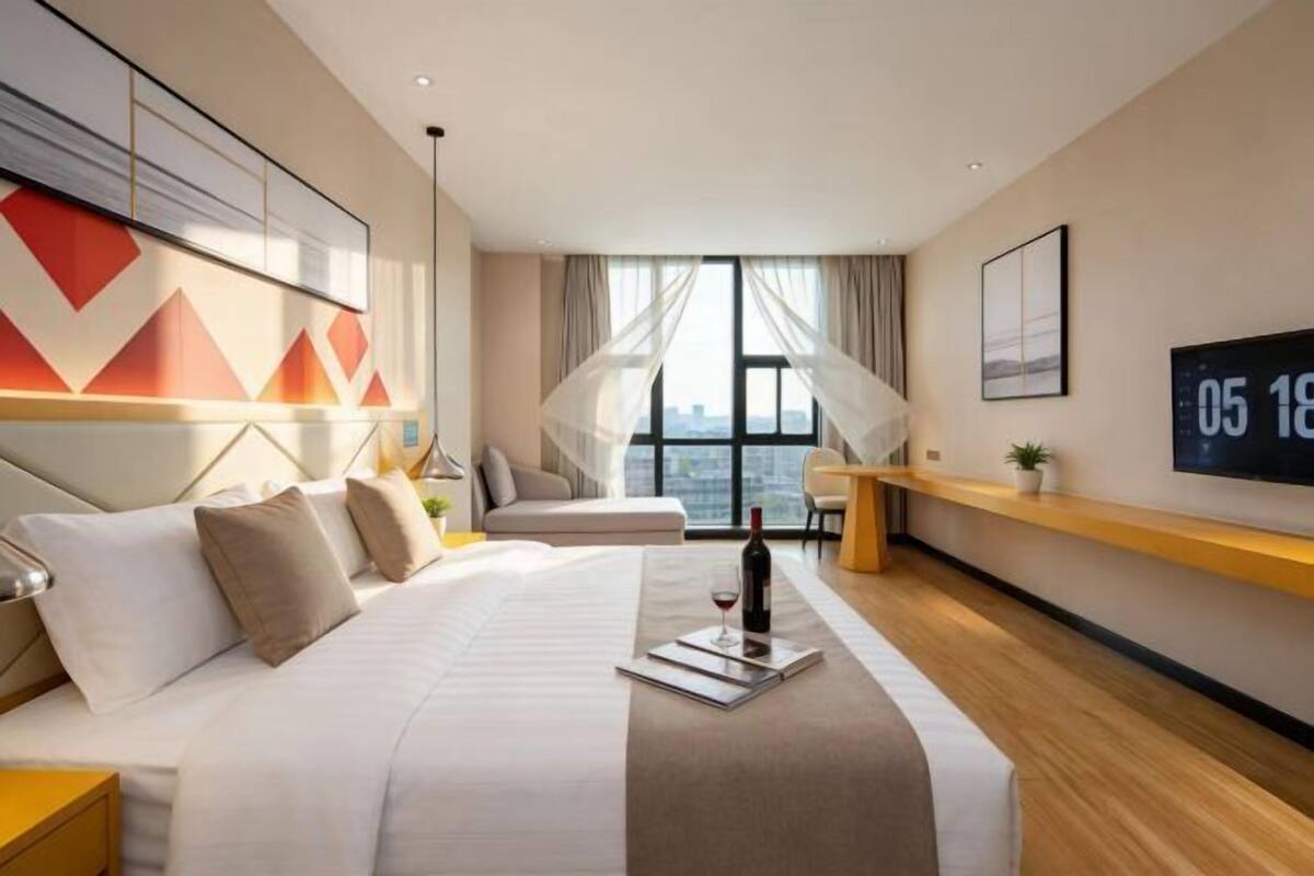Quarto de hotel moderno com uma cama grande, uma mesinha de cabeceira, uma televisão e vista para a cidade.