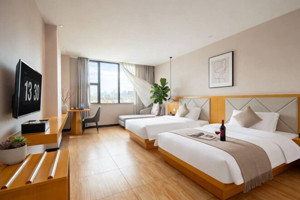 Quarto de hotel com duas camas, uma escrivaninha, televisão e vista para a cidade.