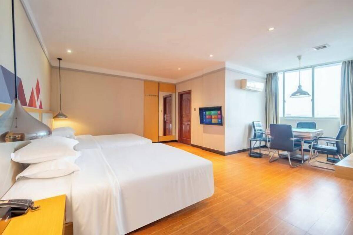 Quarto de hotel com duas camas, uma escrivaninha com cadeira, televisão e janela com cortinas.