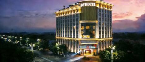 A multi-story hotel with a prominent 'BYHOTEL' sign, featuring a modern architectural design with a central atrium and a reflective pool in front.