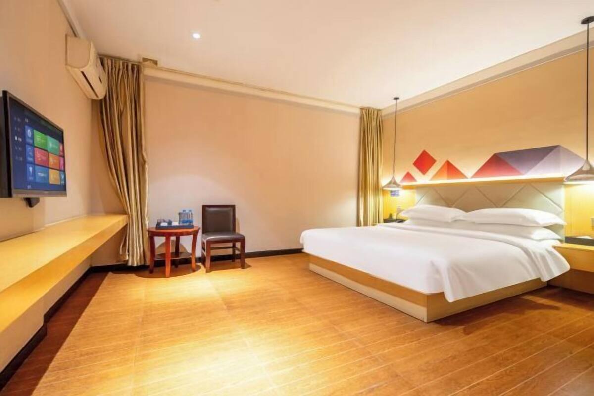 Quarto de hotel com cama, escrivaninha, cadeira, televisão e ar condicionado na parede.